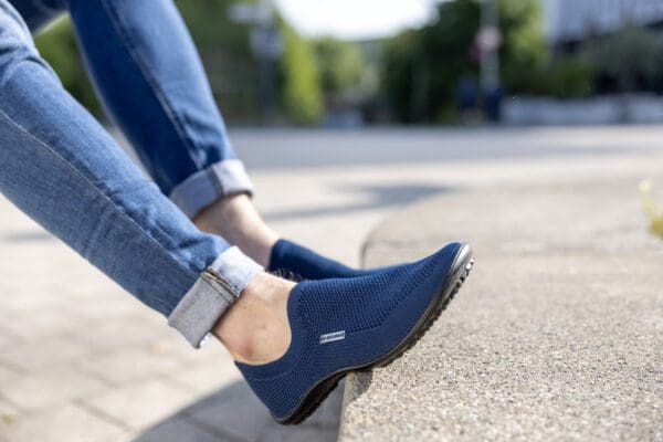 A person wearing blue shoes and jeans on the sidewalk.