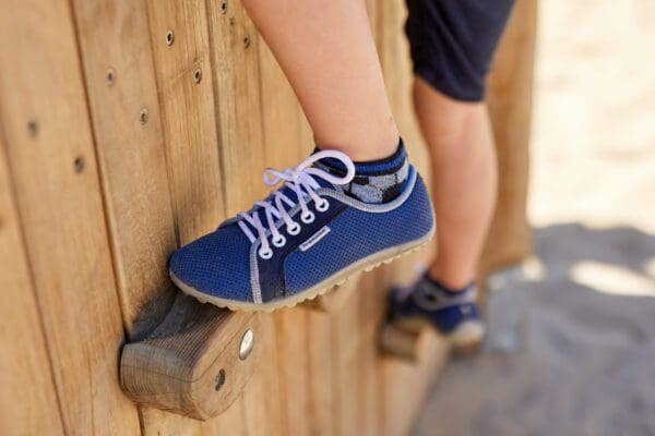 A person with blue shoes is standing on the side of a wooden fence.