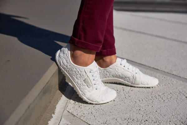 A person wearing white shoes on the side of a street.